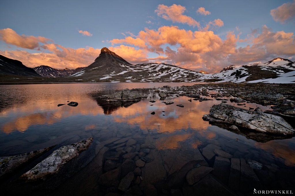 leuchtende orange wolken am blauen himmel über see und vor bergkulisse