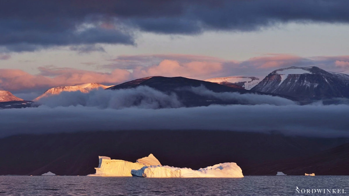 eisberg vor bergern unter zwei wolkjenschichten im abendlicht