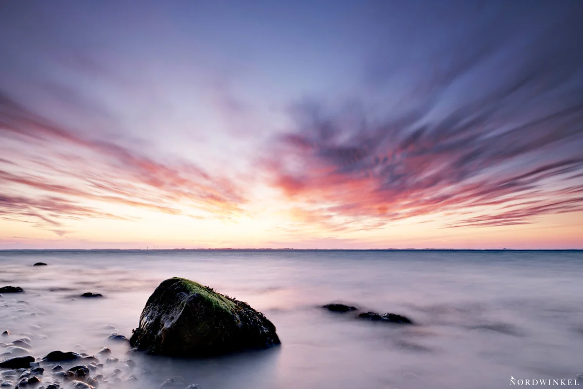 ostsee zum sonnenuntergang fotografiert mit langer belichtungszeit mit glattem wasser und verschwommenen rot leuchtenden wolken, stein als fixpunkt