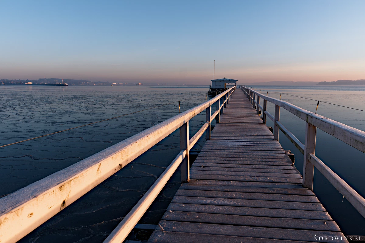 steg am meer führt zu kleinem häuschen über gerfrorenem wasser am morgen