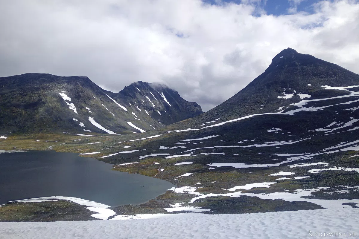 viele wolken über hochgebirge mit see und schneefeldern