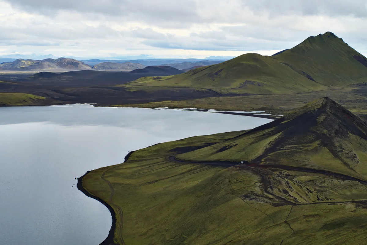 see mit grün bemoosten vulkanbergen in island. kleines auto fährt auf schotterpiste