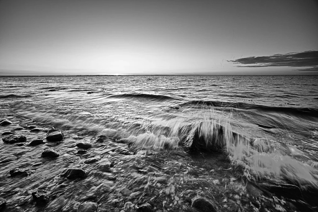 brechende welle über steinen am meer zum sonnenuntergang schwarz weiß