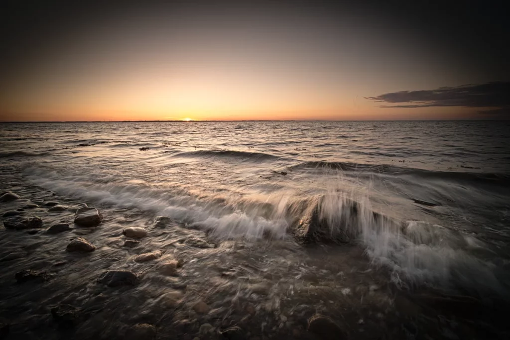 brechende welle über steinen am meer zum sonnenuntergang mit dunklem rand
