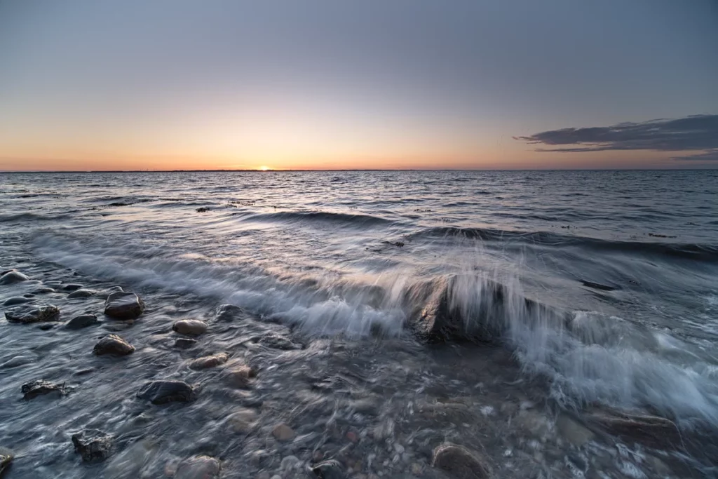 brechende welle über steinen am meer zum sonnenuntergang