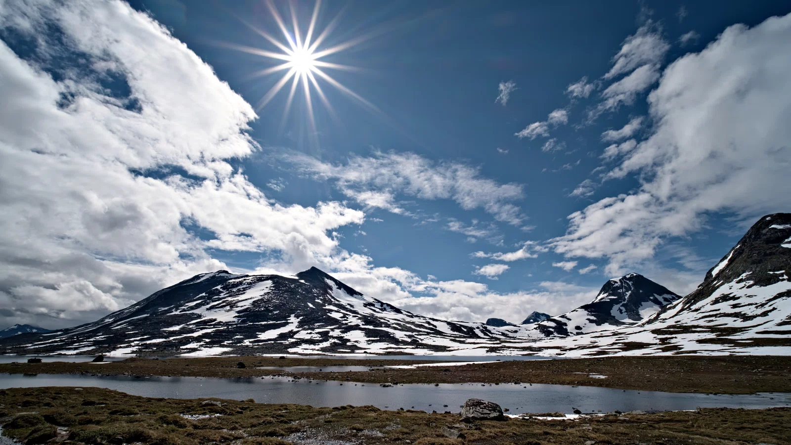 sonne als stern über gebirgslandschaft mit schnee und see durch geschlossene blende