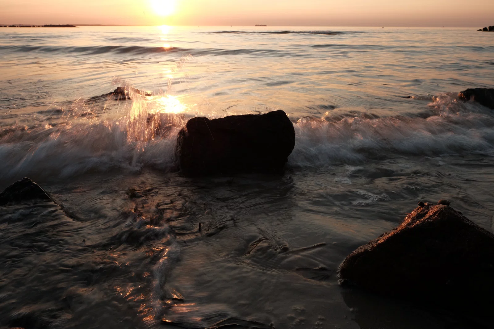 jpeg bild einer welle am steinstrand zum sonnenuntergang