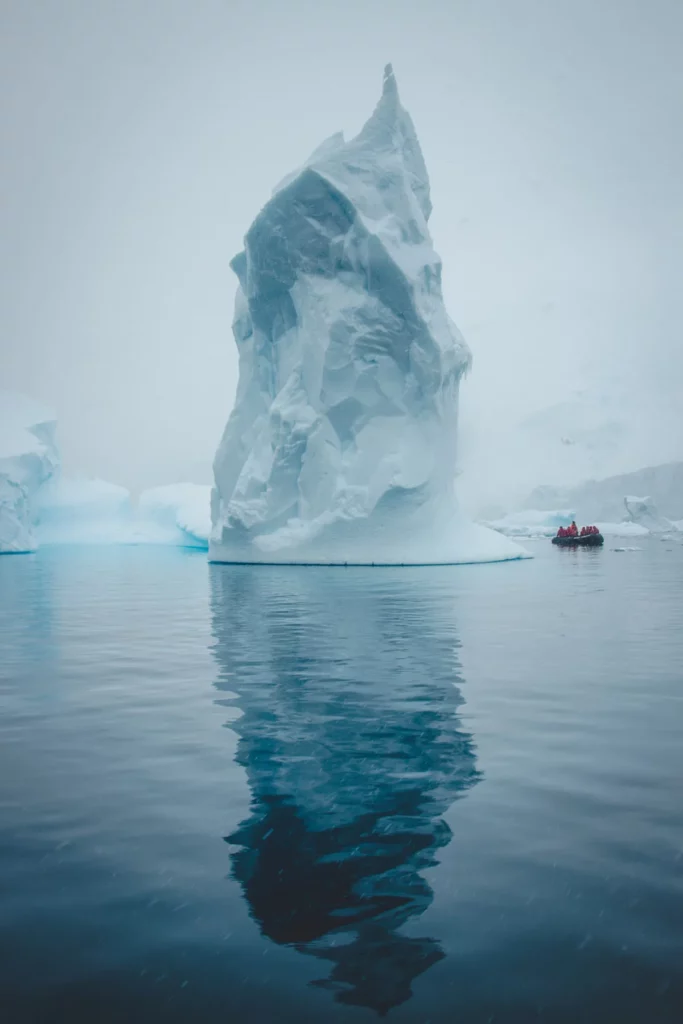 riesiger Eisberg im nebel in der antarktis daneben rechts ein schlauchboot