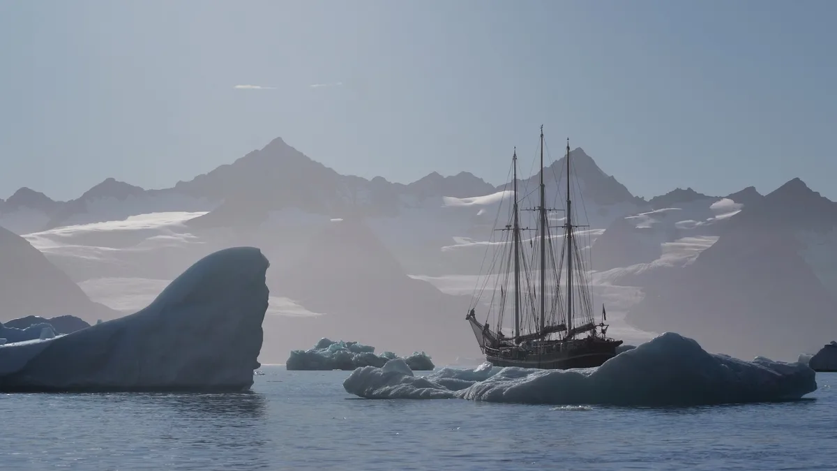 Segelschiff zwischen eisbergen im sonnenlicht vor bergkulisse