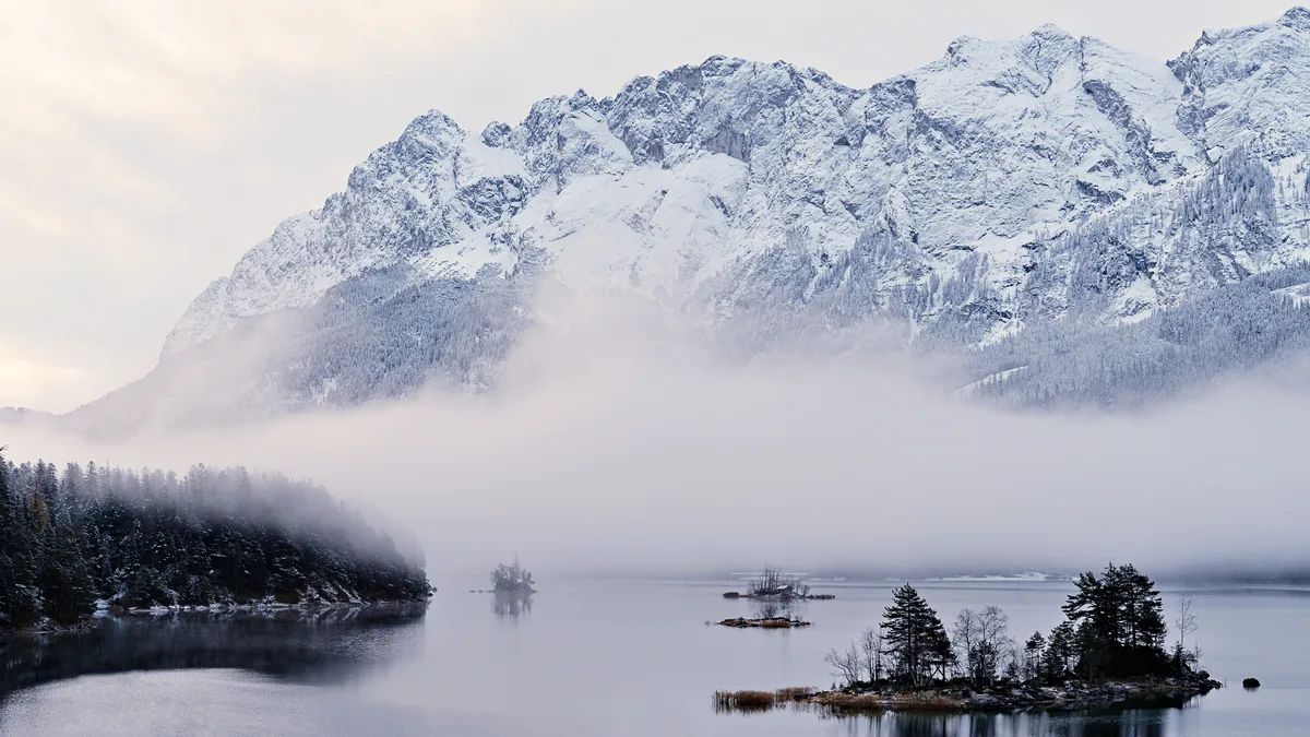 bergwand vor eibsee mit inseln im wasser und nebelschwaden