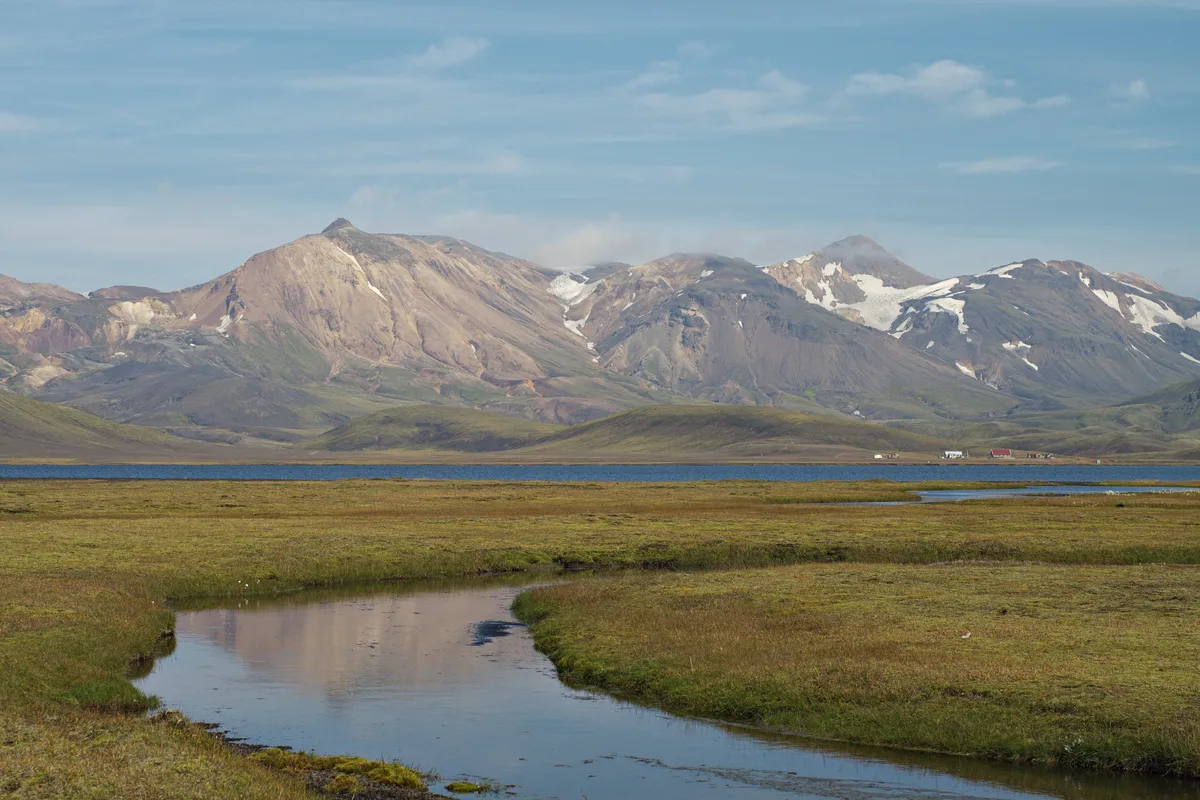 fluss im vordergrund, dahinter ein see und im hintergrund hohe schneebedeckte berge auf island