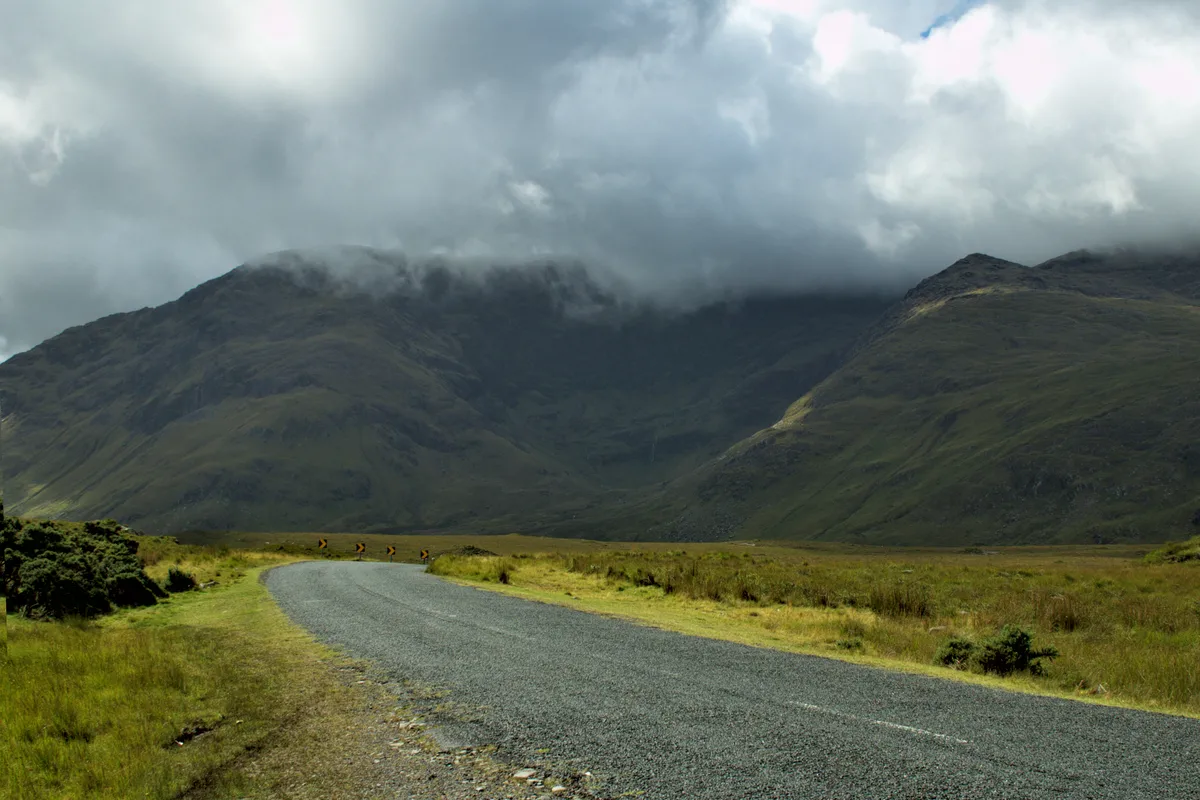 straße in irland führt in rechts kurve auf wolkenverhangene berge zu