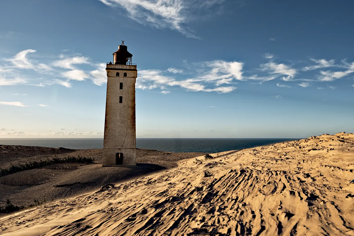 leuchtturm in sanddüne mit blauem himmel und wolkenband im goldenen schnitt