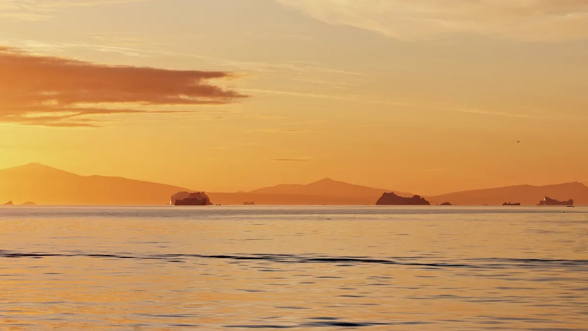 grönländische küste mit eisbergen im wasser in goldenem licht zur goldenen stunde