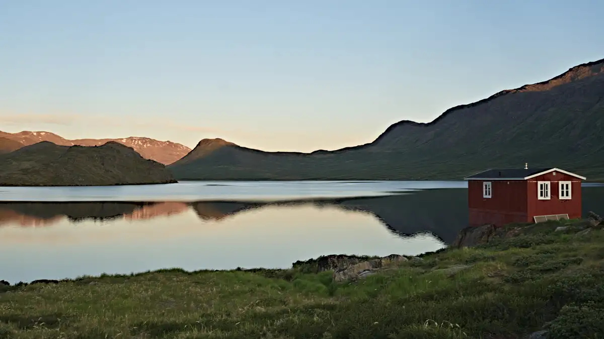 rote hütte in grönland an einem ruhigen see zum sonnenuntergang mit hügeln im hintergrund