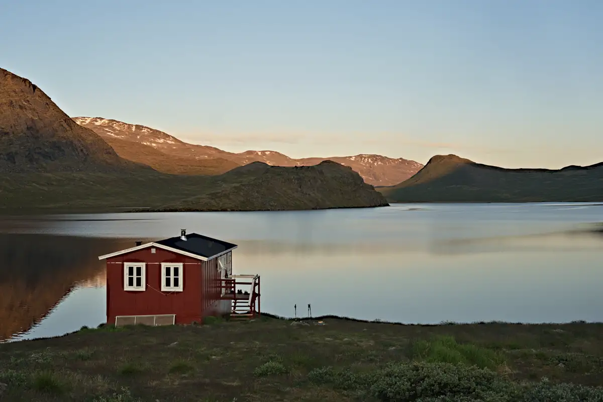 kleine rote hütte am see zum sonnenuntergang mit bergen im hintergrund
