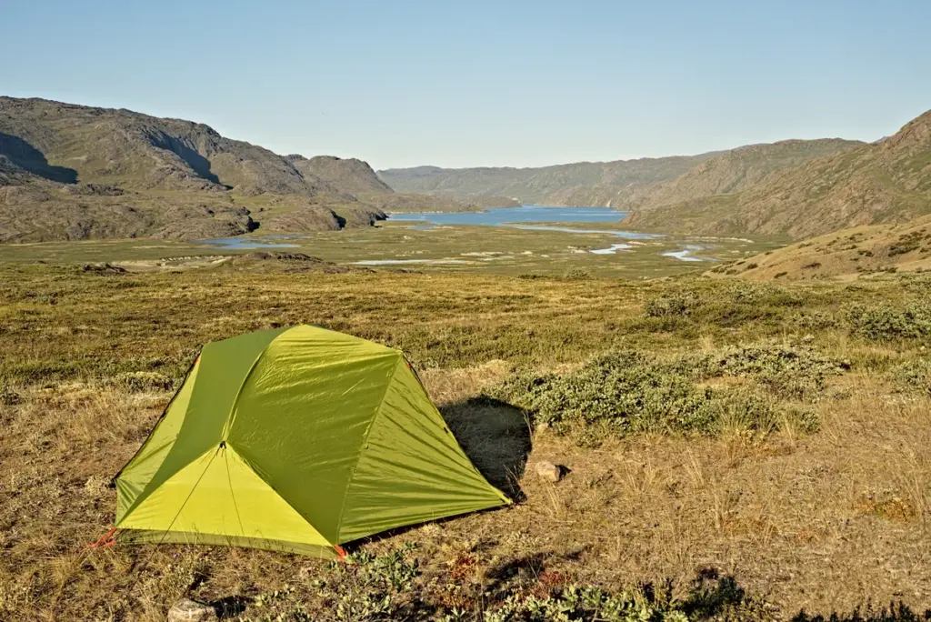 zelt in der arktischen tundra mit ausblick auf fjord am horizont