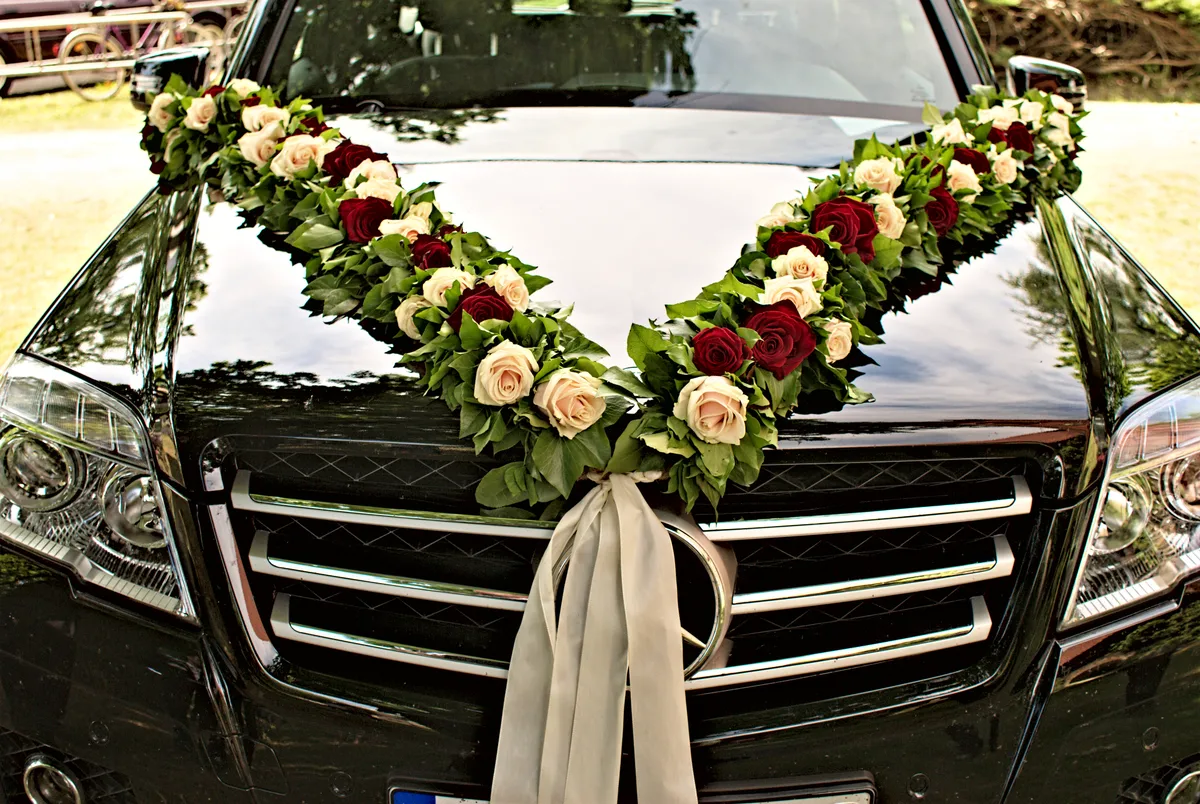 girlande aus weißen und roten rosen mit grünen blättern auf der motorhaube eines autos